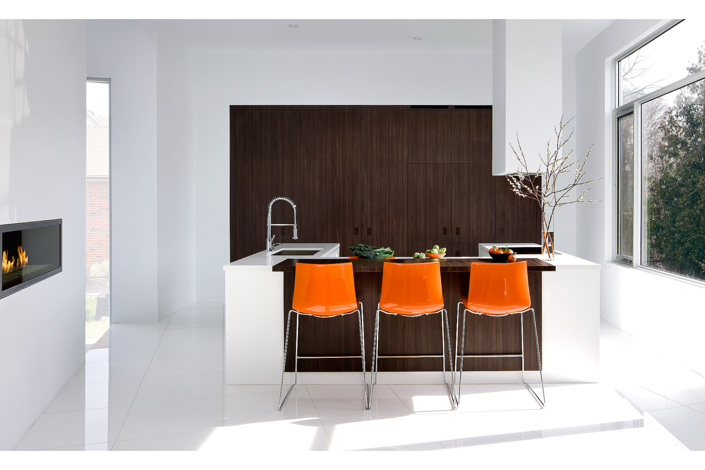 an interior photograph of a minimalist styled kitchen with vibrant orange chairs